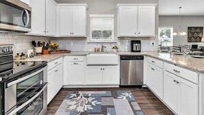 Una cocina moderna con armarios blancos, electrodomésticos de acero inoxidable y una alfombra estampada.