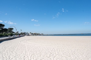 Ein weiter Sandstrand mit blauem Himmel, einem entfernten Pier und einem Riesenrad.