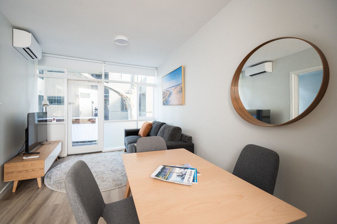 A modern living room with a wooden table, grey chairs, a sofa, and a large mirror.