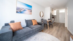 Een moderne woonkamer met een grijze bank, een eettafel met stoelen, en een keuken in de achtergrond.