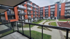Un immeuble résidentiel à plusieurs étages, doté de balcons, d’une cour pavée et d’un espace de jeux pour enfants.