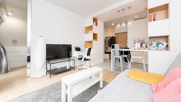 Un salon moderne doté d’un téléviseur à écran plat, d’un canapé blanc, d’une table basse et d’un coin repas avec une cuisine en arrière-plan.