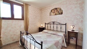 Una camera da letto con un letto, due comodini, una finestra con tende e carta da parati a motivi floreali.