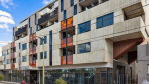Un edificio de varios pisos con un diseño arquitectónico moderno, que presenta balcones, ventanas amplias y una entrada a nivel de calle con puertas de vidrio.
