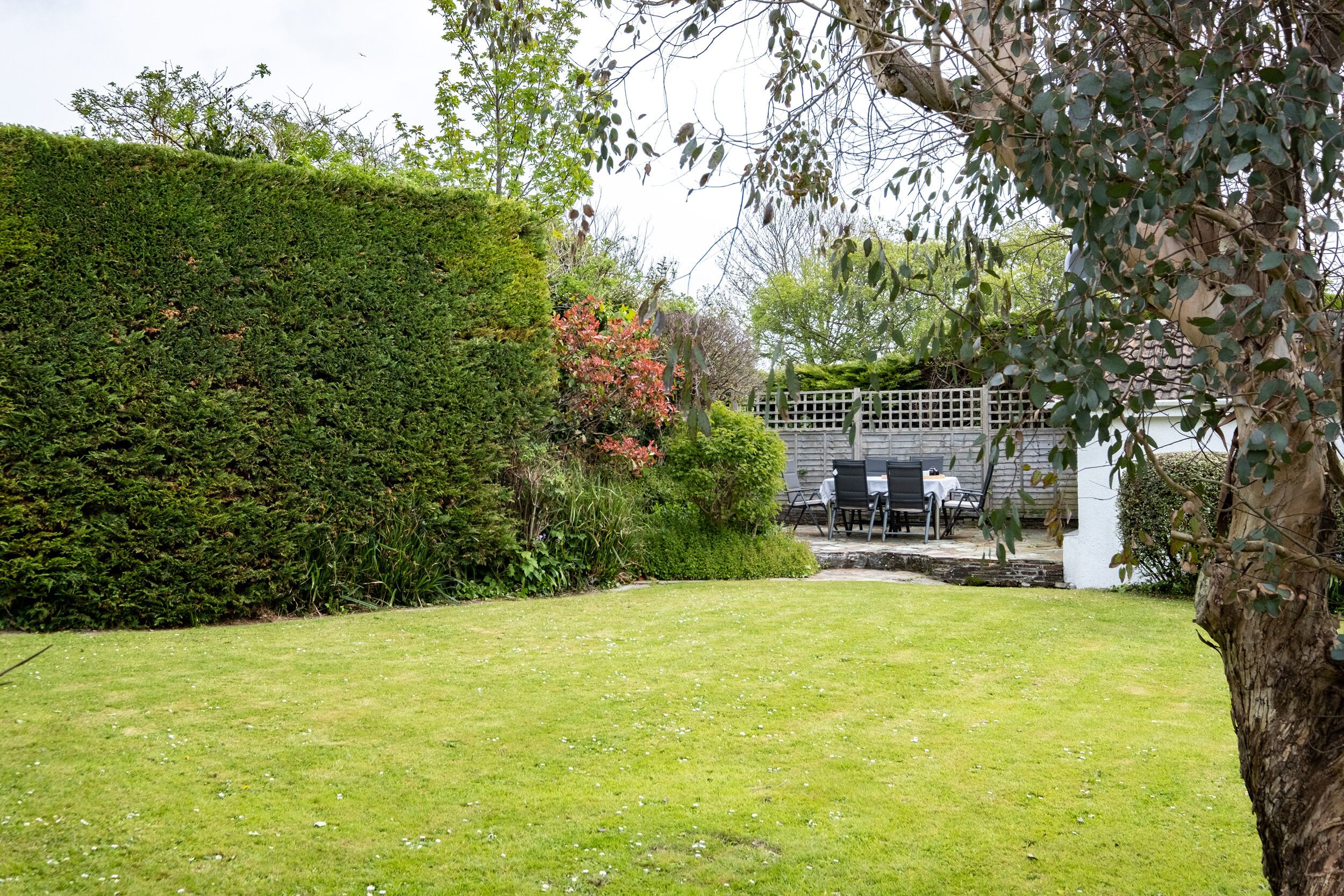 A well-maintained garden with a neatly trimmed hedge, a grassy lawn, and a patio area with outdoor furniture.