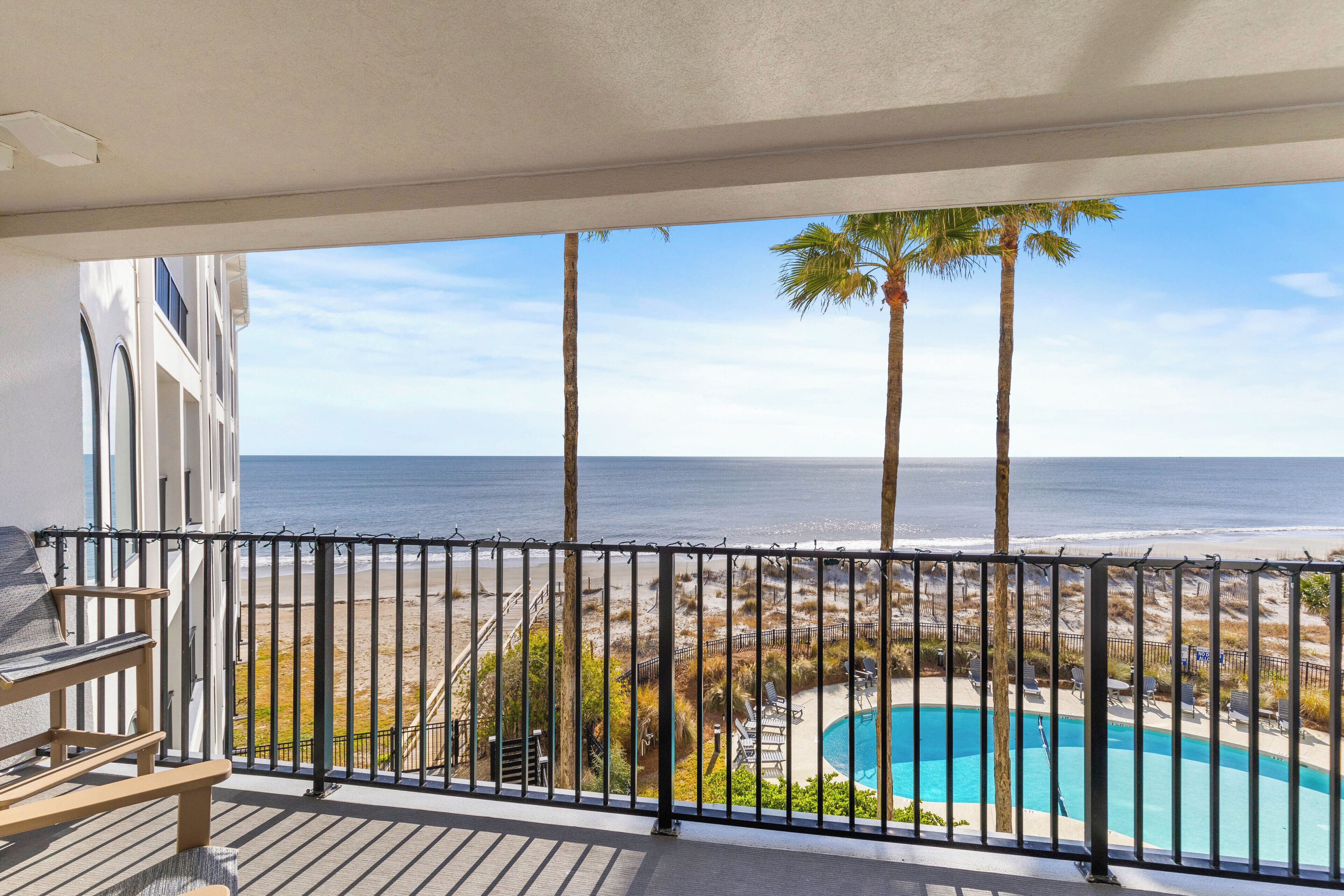 Un balcon avec vue sur la plage et l’océan, une piscine et du mobilier d’extérieur.