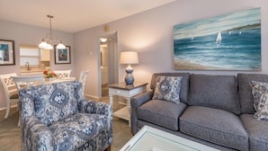 A living room with a gray sofa, patterned armchairs, a dining area with a white table, and a painting of a sailboat on the wall. - Condo#203 Updated beautiful  condo on Siesta Key with an upscale comfortable coastal look and feel. (Sarasota)