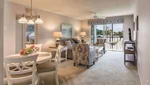 A spacious living area with a dining table, chairs, a sofa, and a patterned armchair. There is a ceiling fan and a large window with a view of the outdoors. - Condo#203 Updated beautiful  condo on Siesta Key with an upscale comfortable coastal look and feel. (Sarasota)