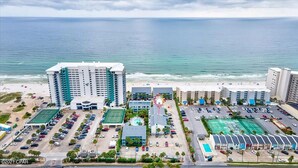 Complejo hotelero frente al mar con varias construcciones, un estacionamiento y una playa al fondo.