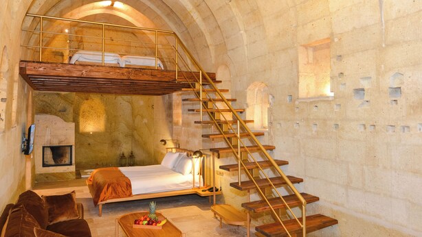 Una habitación con una cama, un banco de madera, una pequeña mesa con fruta, un sofá y una escalera.