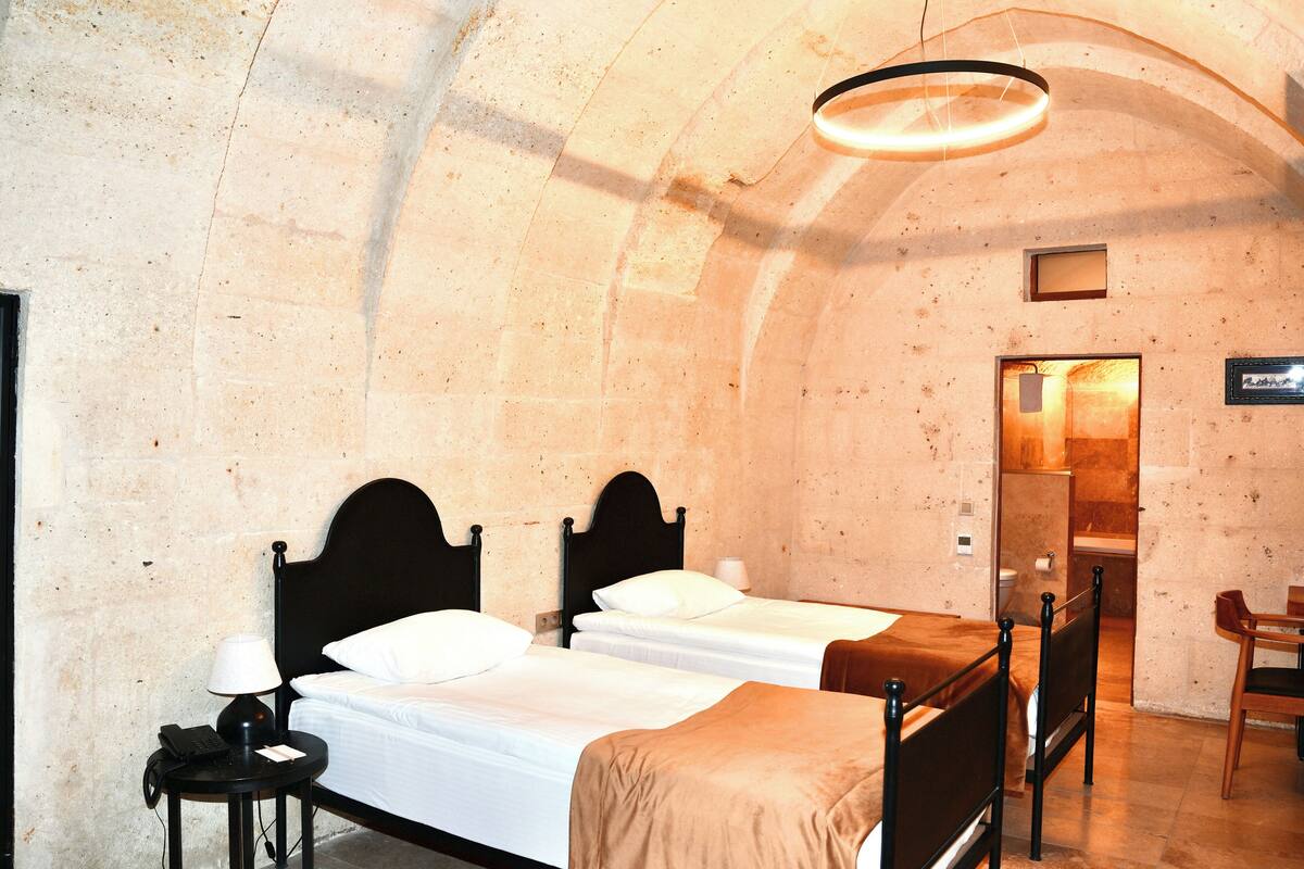 A room with two beds, a desk with a lamp, a chair, and a bathroom door.