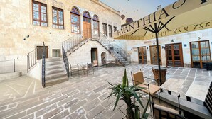 Un patio con suelo de piedra, una escalera, mobiliario exterior y un edificio con ventanas de arco y un letrero.