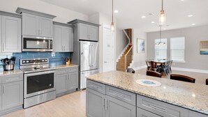 Una cocina moderna con encimeras de granito, electrodomésticos de acero inoxidable y un comedor con mesa y sillas de madera.