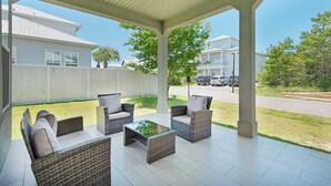 Un patio techado con mobiliario de mimbre y una pequeña mesa, con vistas a una calle residencial.