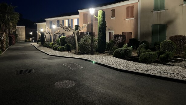 Ein Nachtbild einer Straße mit einer Reihe von Gebäuden, jedes mit einem eingeschossigen Bau, mit einem zentralen Weg, der von gepflegten Büschen und einer Pflasterkante gesäumt wird.