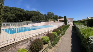 Ein Schwimmbecken mit weißem Zaun, umgeben von Grünpflanzen und einem Weg.