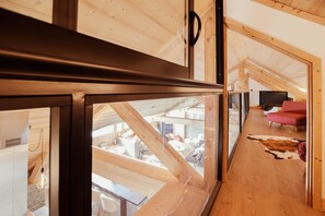Um interior moderno com uma porta de vidro que dá para um espaço tipo loft com vigas de madeira, uma televisão e uma cadeira vermelha.
