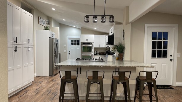 A modern kitchen with white cabinets, a central island with bar stools, stainless steel appliances, and a hanging light fixture.
