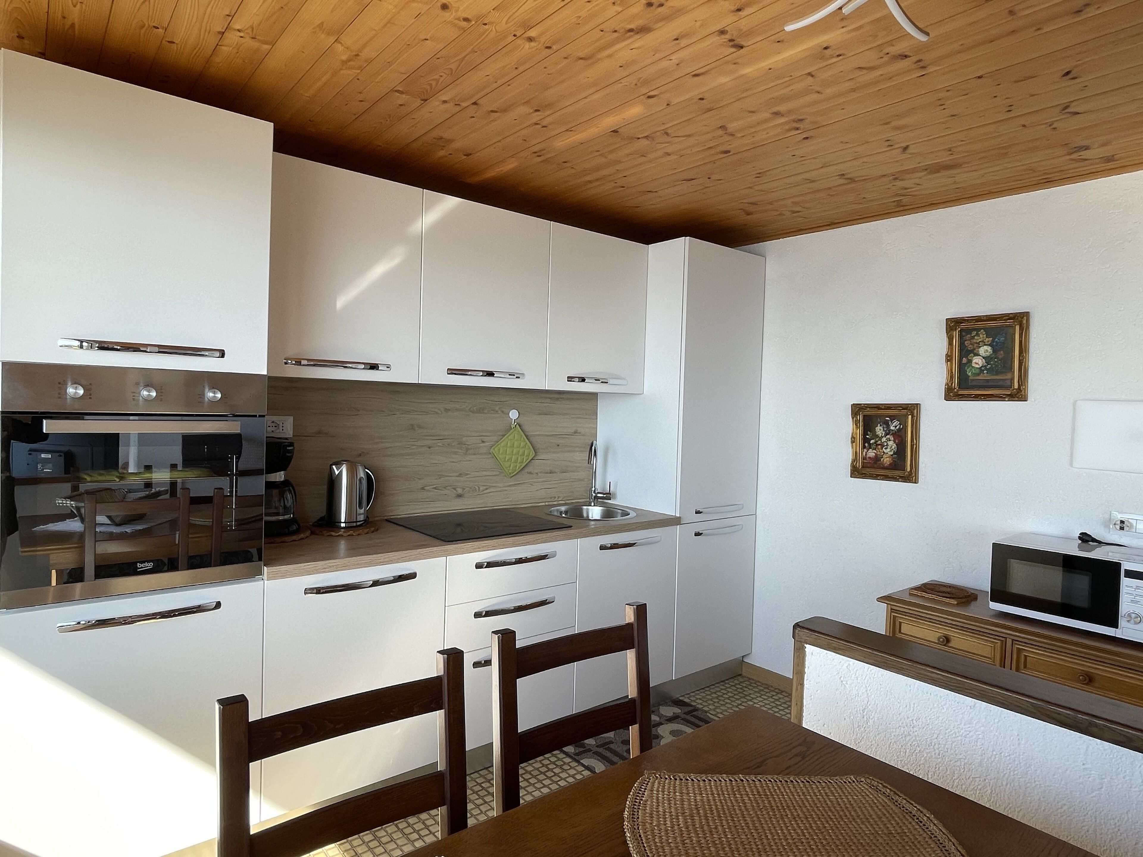 A compact kitchen with white cabinets, a wooden ceiling, a microwave, and a kettle.