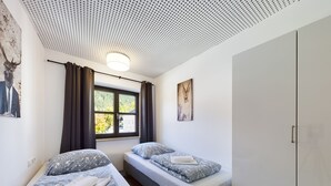 Un dormitorio con dos camas, una ventana con cortinas, un techo con diseño perforado y un armario.