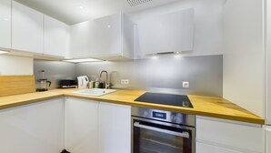 Una cocina moderna con armarios blancos, encimera de madera, un fregadero, una tetera, una cafetera y un horno.
