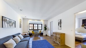 Una sala de estar moderna con un sofá, un comedor con sillas, una alfombra azul y obras de arte en las paredes.