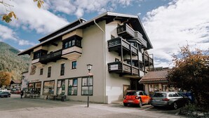 Un edificio de varios pisos con balcones, una tienda en la planta baja y coches estacionados al frente.