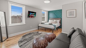Una camera da letto moderna con un letto, una TV, una poltrona e una finestra con tende.