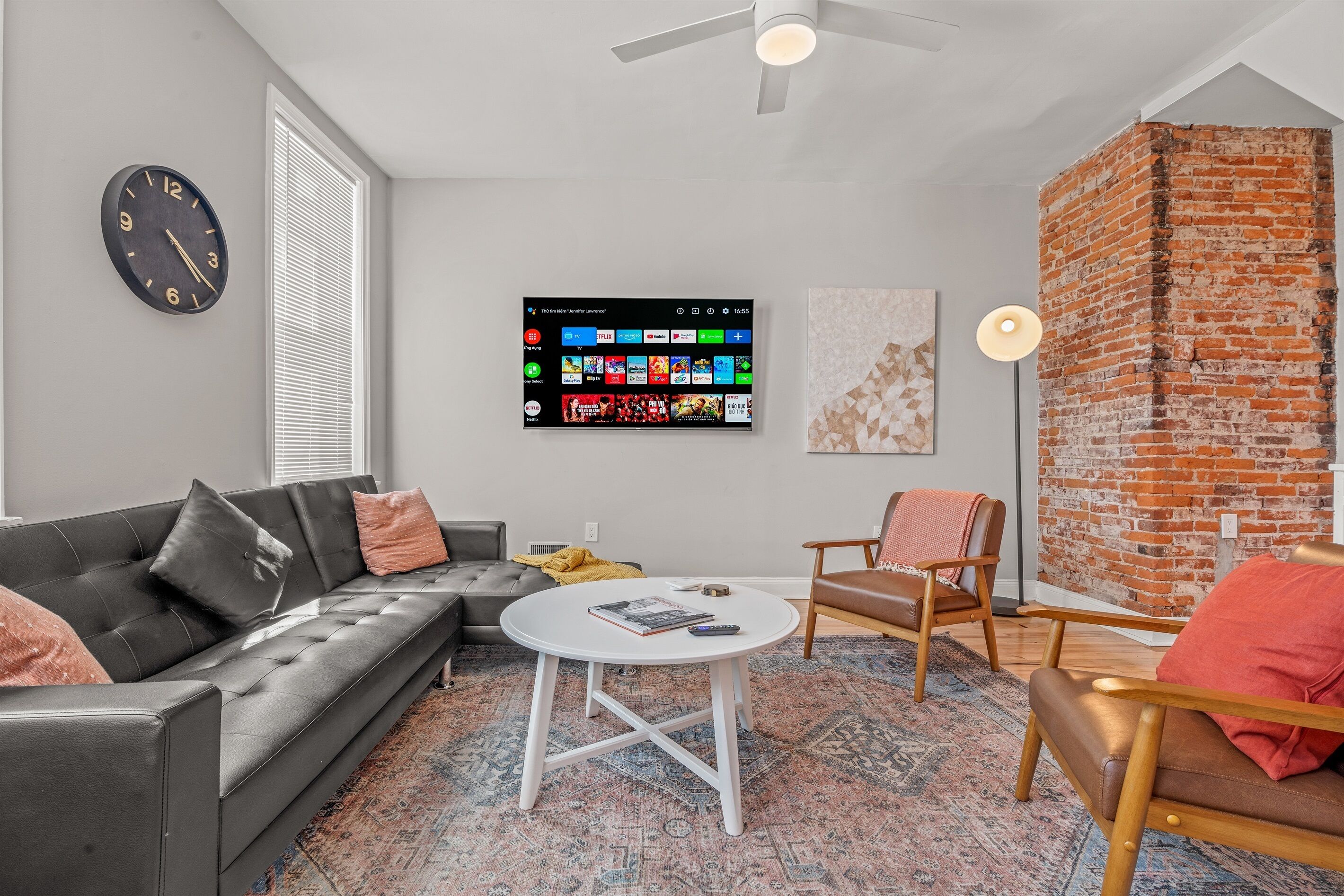 A modern living room with a sectional sofa, a coffee table, a TV mounted on the wall, and a brick accent wall.