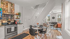 Una cucina moderna con piano cottura, forno e pensili bianchi. C'è una zona pranzo con tavolo e sedie. Una scala conduce a un altro livello.