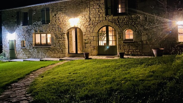 Un edificio de piedra con fachada de piedra, varios ventanales de arco y un área de entrada pavimentada.
