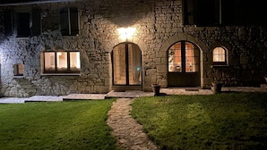 Un edificio de piedra con una entrada bien iluminada, un camino de piedra que lleva a la puerta y un césped delantero.