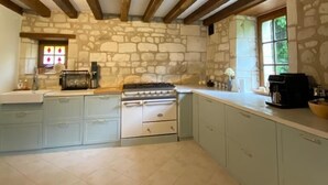 Una cocina con paredes de piedra, vigas de madera, estufa a gas y armarios azul claro.