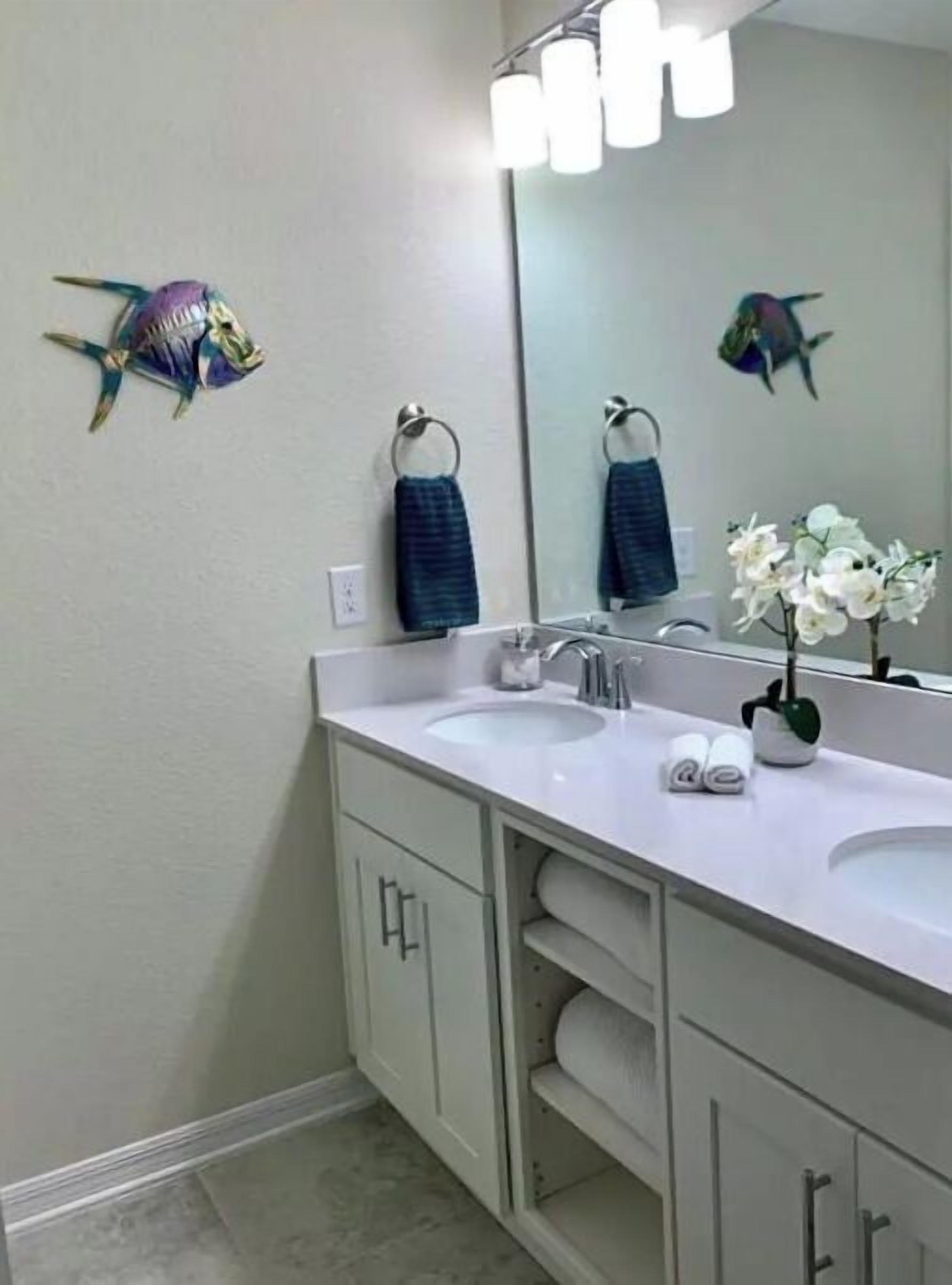 A bathroom with two sinks, a large mirror, and decorative fish on the wall.