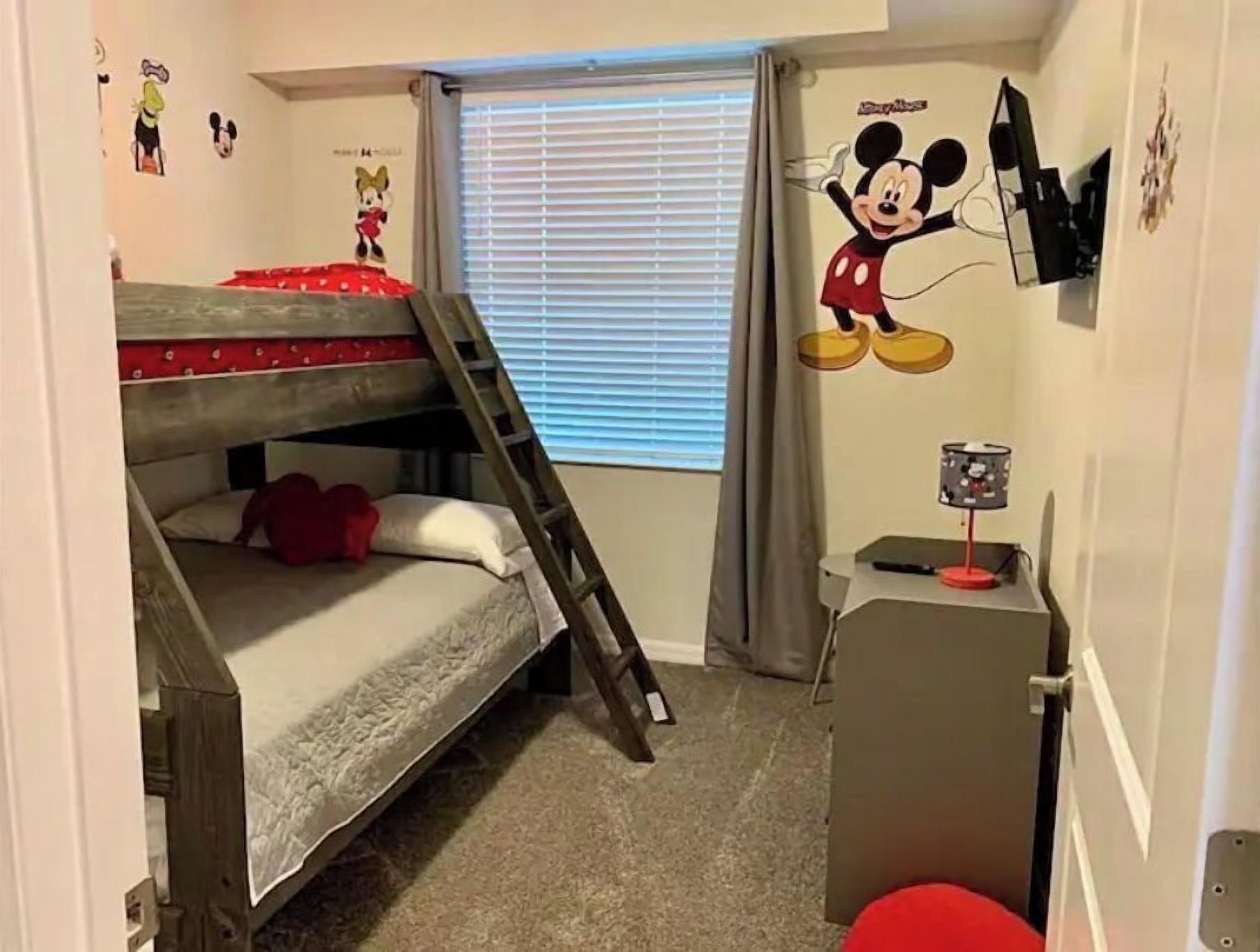 Quarto compacto com beliche, escrivaninha e janela com cortinas.