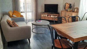 Una sala de estar con un sofá, una mesa de centro, un televisor y una mesa de comedor con sillas.