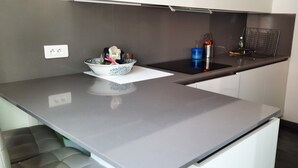 Una cocina moderna con encimera gris, un bol con tapa blanca, un recipiente azul y una rejilla metálica.