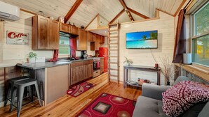 A cozy cabin interior with wooden floors, a kitchen with a red refrigerator, a dining area with a red rug, and a living room with a gray sofa. - The 'Happy Go Fishing Cabin' at the Park Place (on Parks Rd)  (Woodleaf)