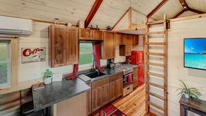 A compact kitchen with wooden cabinets, a red refrigerator, and a coffee-themed sign. - The 'Happy Go Fishing Cabin' at the Park Place (on Parks Rd)  (Woodleaf)