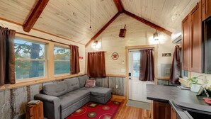 A cozy cabin interior with a wooden ceiling, a gray sectional sofa, a red patterned rug, and a kitchen area with a countertop and cabinets. - The 'Happy Go Fishing Cabin' at the Park Place (on Parks Rd)  (Woodleaf)