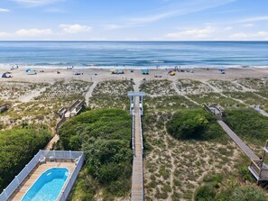 A beach with a wooden boardwalk leading to a pool area, surrounded by dunes and beach umbrellas. - Classic oceanside home offering private pool and easy beach access. (Emerald Isle)