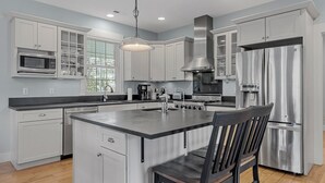A modern kitchen with white cabinetry, a central island, stainless steel appliances, and a dining area with a chair.