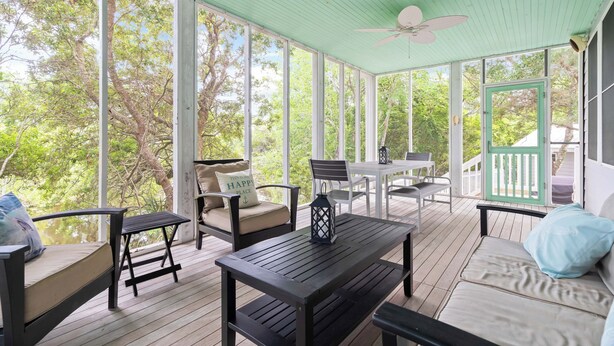 A covered porch with wooden flooring, a ceiling fan, and large windows offering a view of trees.