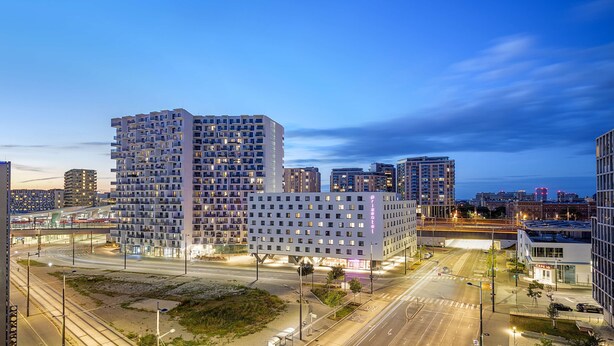A modern hotel with a grid of rooms, a central atrium, and a view of the surrounding cityscape at dusk. - Prize by Radisson, Vienna City (Vienna)