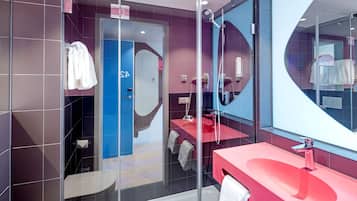 A modern bathroom with a glass shower enclosure, a red sink, and a large mirror.