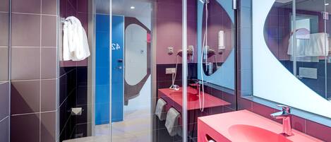 Un baño moderno con cabina de ducha de vidrio, un lavamanos rojo y un espejo grande.