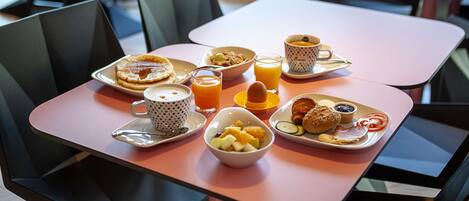 Une table de petit-déjeuner avec des assiettes remplies de nourriture, un verre de jus d’orange et une tasse de thé.