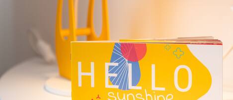 Una lámpara amarilla abstracta con un libro titulado "HELLO Sunshine" sobre una superficie blanca.