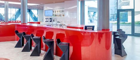 A modern bar area with a red counter, black bar stools, and a large window offering a view of the outside.