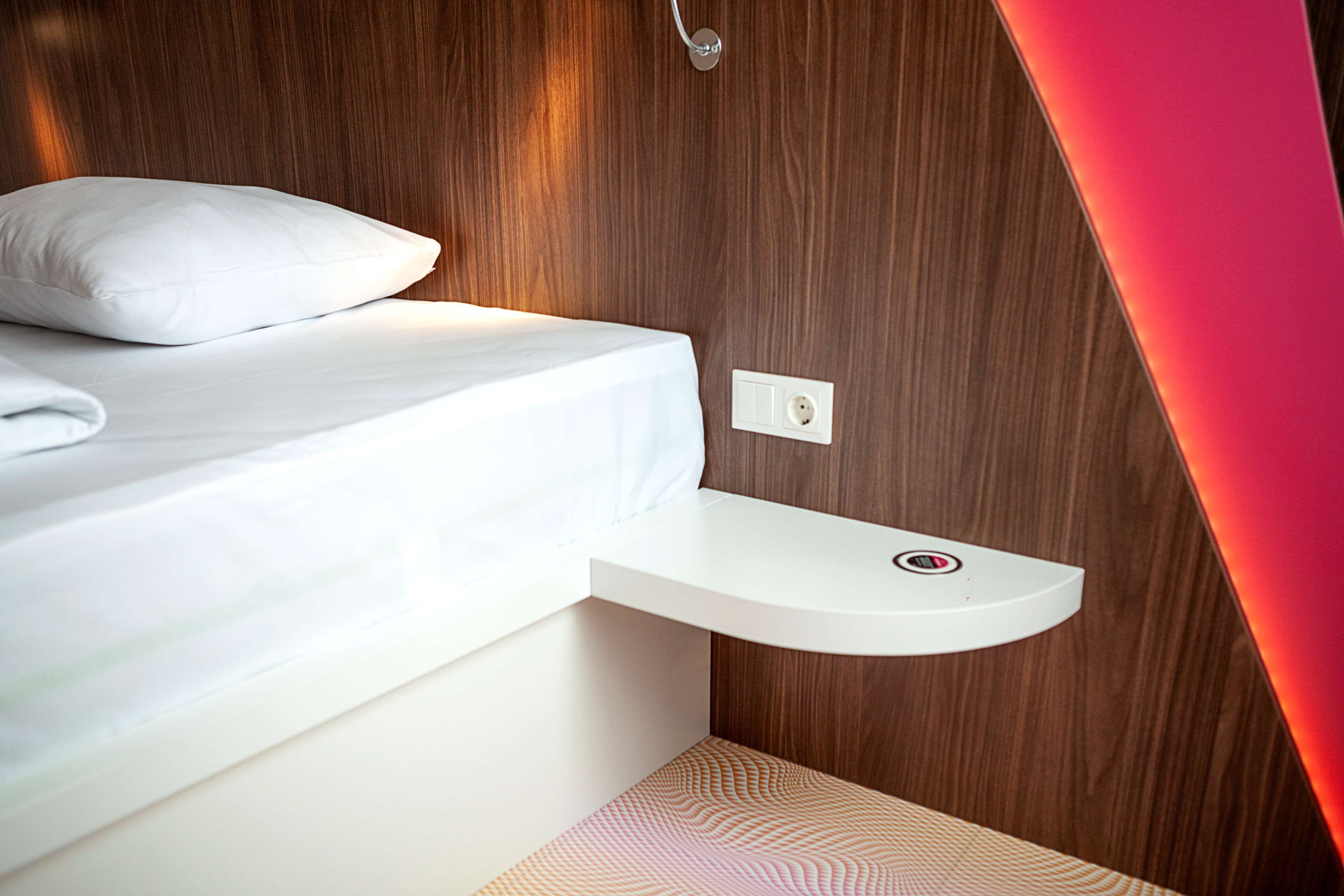 A modern bedroom with a bed, a bedside table, and a wall-mounted light fixture.